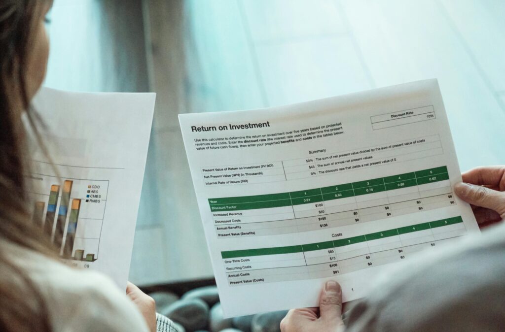 Two people reviewing a financial document titled "Return on Investment" which includes a summary, discount rates, and tables for benefits and costs.